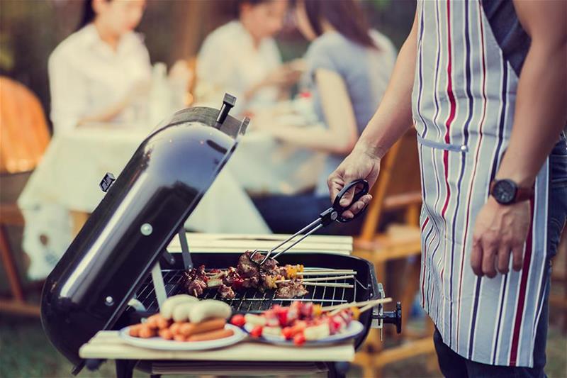 An individual grilling meat and vegetables at a gathering