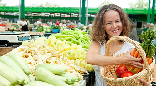 A woman at a Farmer's Market filling her basket with vegetables