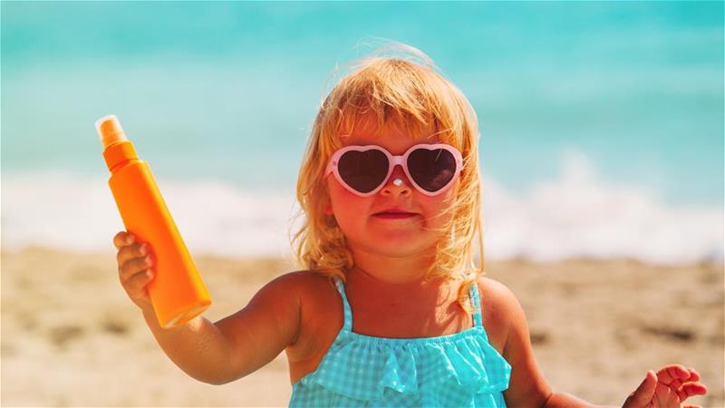 A little girl on the beach holding up a sunscreen bottle