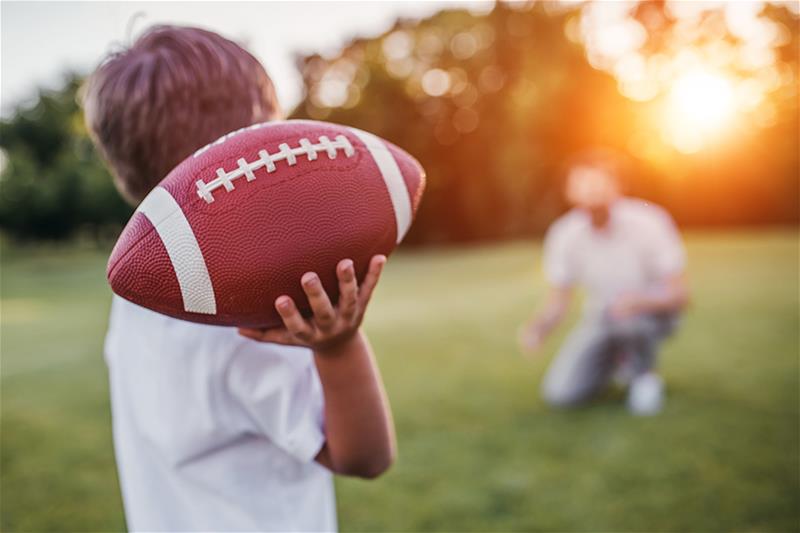 A young boy throwing the football to his dad outside