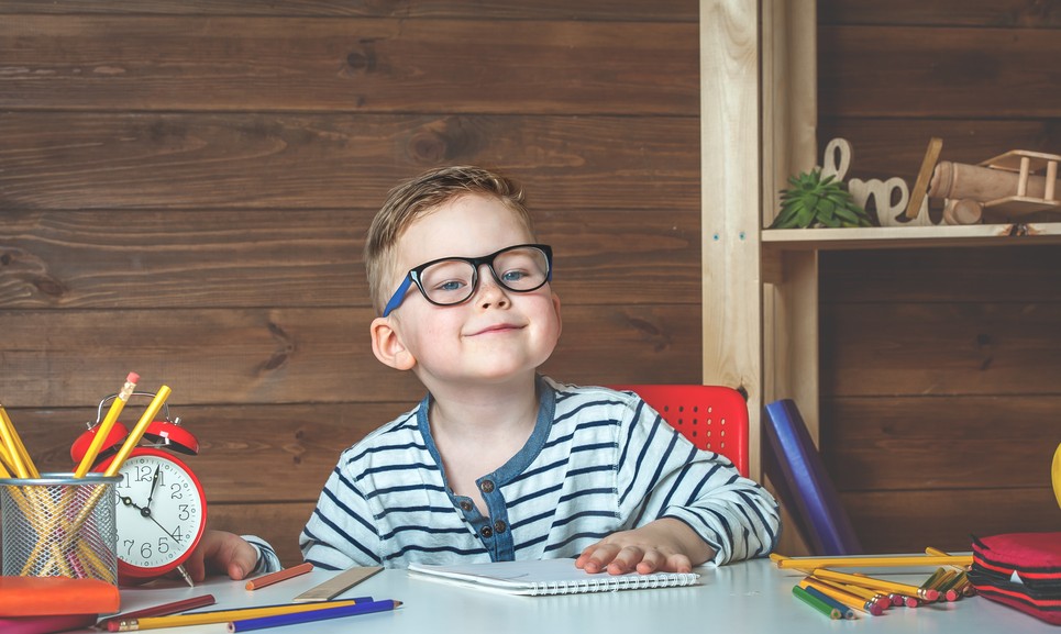 A little boy at a table with supplies and a clock