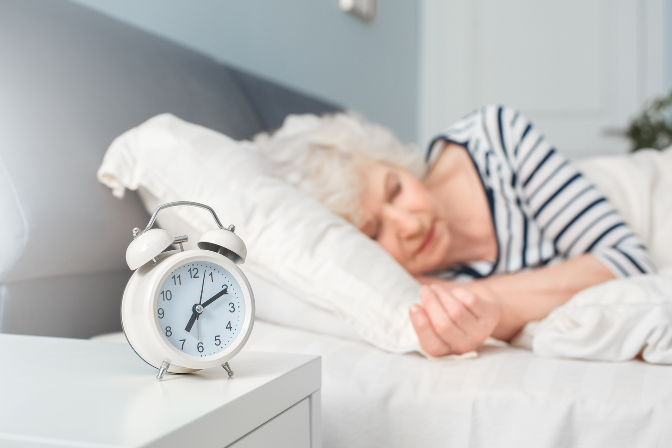 An elder woman sleeping with an alarm clock in the foreground