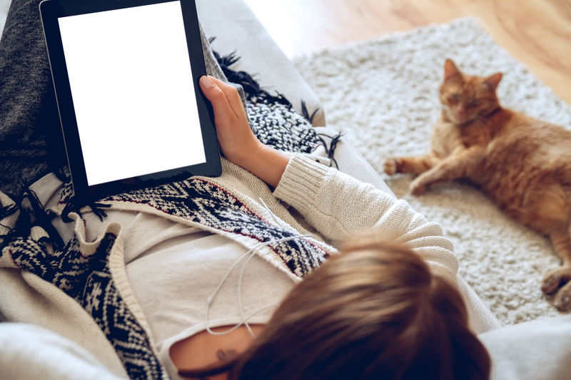 A woman lying on the floor with her cat using her tablet