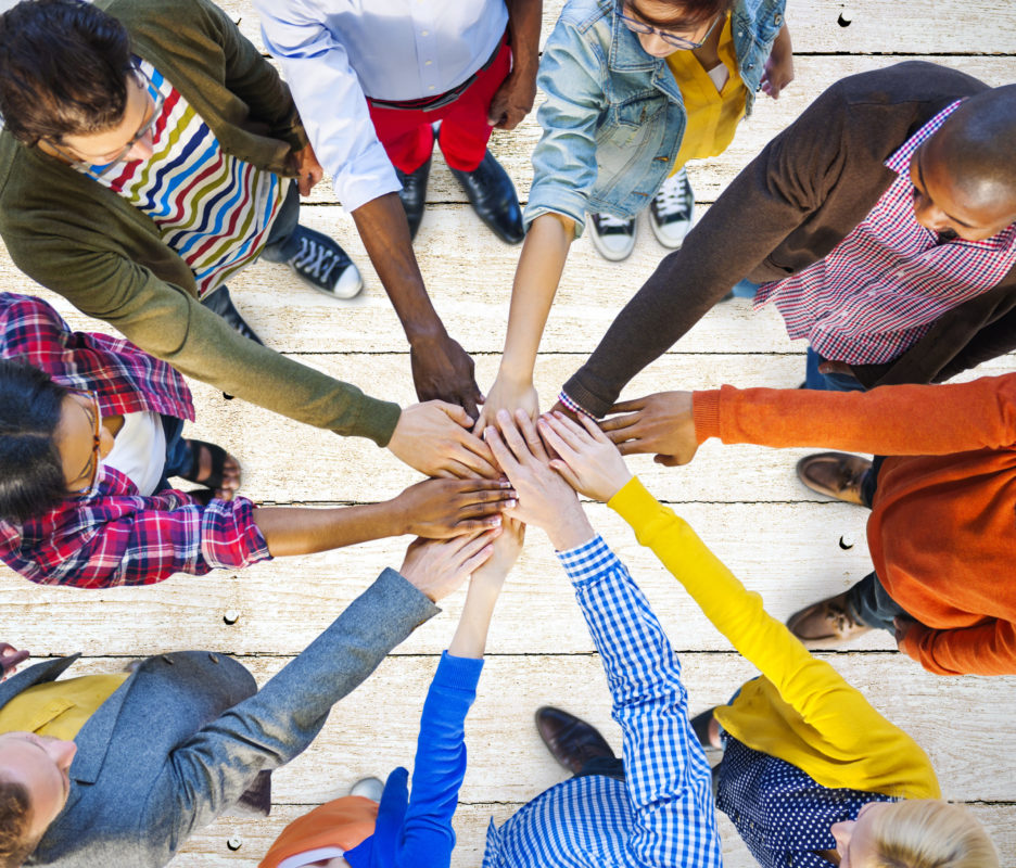 A diverse group of people in a circle with their hands in the middle