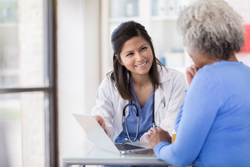 A doctor talking to an older woman with records on her laptop