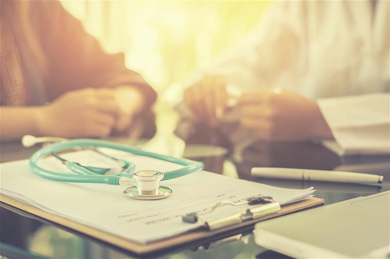 A doctor and patient sitting with a stethoscope and clipboard on the table