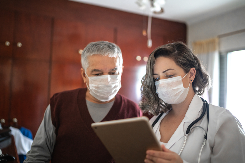 A healthcare professional talking to a senior patient and using a laptop