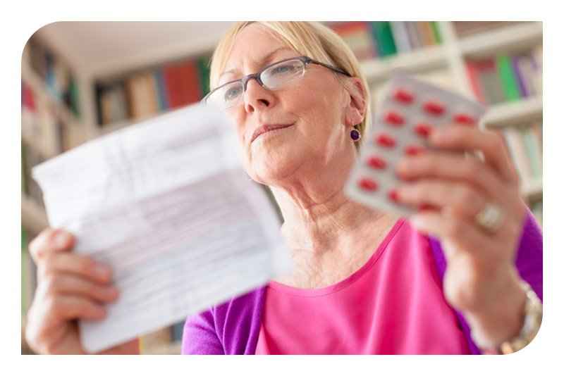 A senior woman holding pills in one hand and reading prescription information in the other