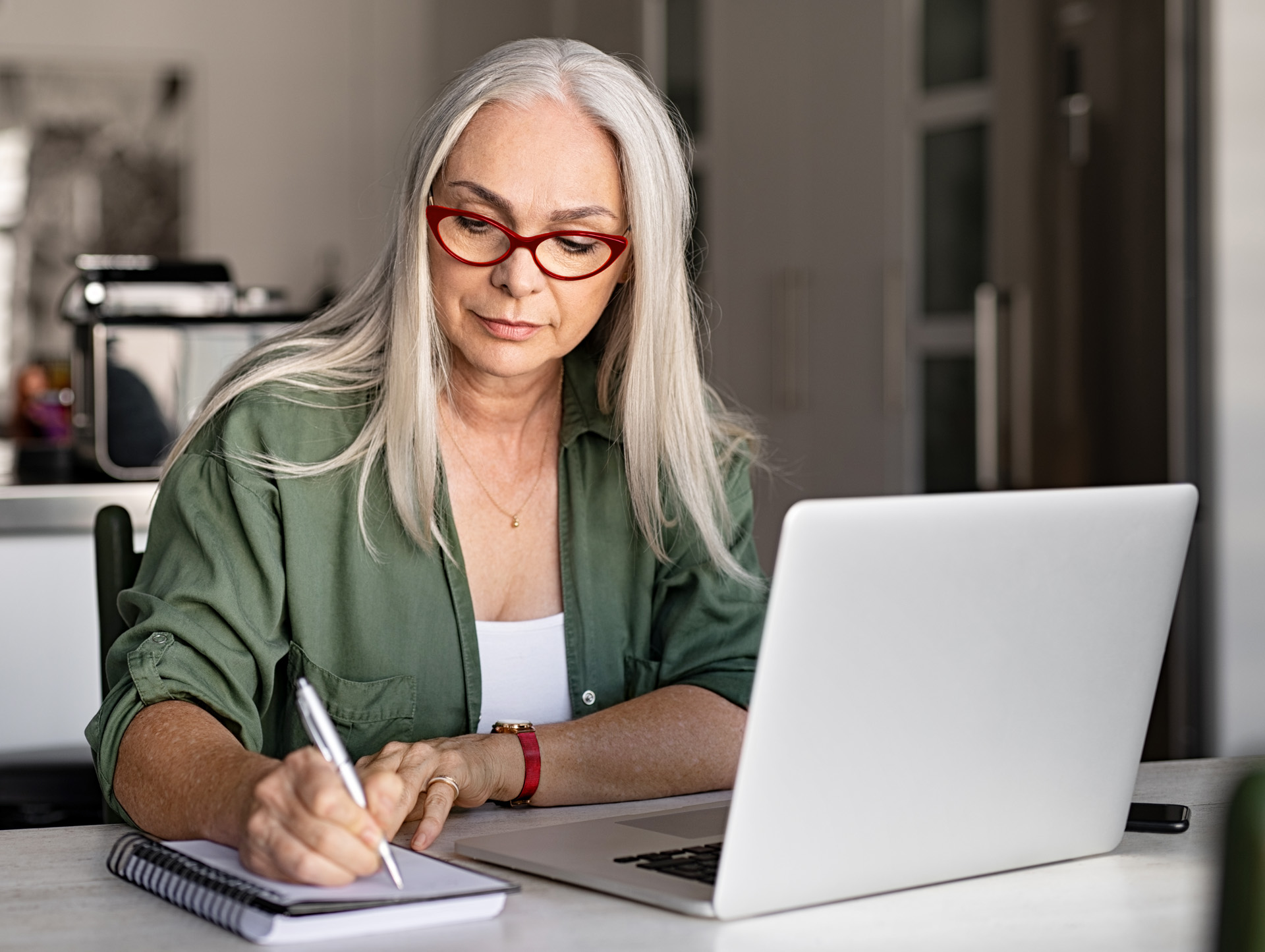 A senior woman writing on a notebook at her desk