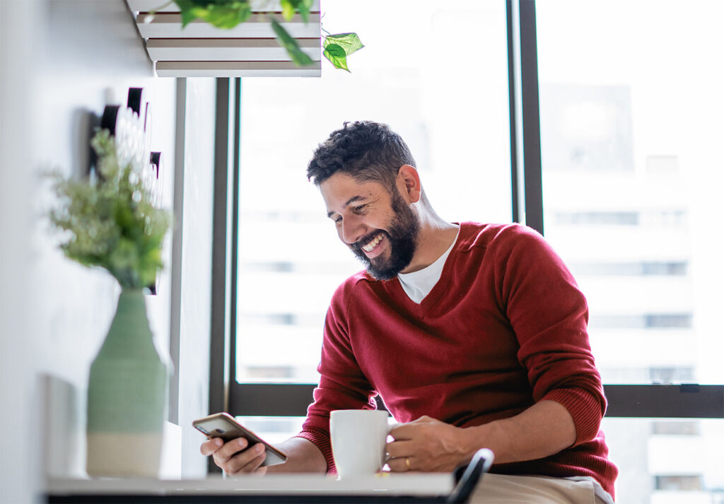 A man using his smartphone and holding a coffee mug